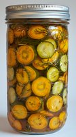 Homemade pickled carrots and cucumbers with fresh dill in glass mason jar. Close up view of preserved vegetables in brine marinade showing texture and detail.