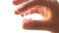 Transparent glass tube held between human fingers against bright backlit background, isolated on white for design use.
