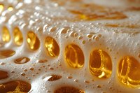 Golden liquid droplets with white foam creating abstract macro photography pattern. Refreshing beverage bubbles catching light in amber tones against blurred background.