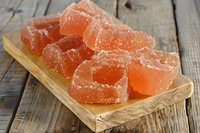 Orange sugar-coated jelly candy cubes arranged on wooden serving board against rustic wooden background, sweet homemade confectionery dessert treat.