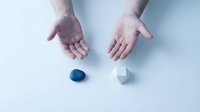 Hands reaching toward blue and white pills on clean surface representing healthcare choice and medication decision concept.