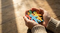 Hands holding colorful paper cutout figures representing diversity, community support, teamwork and social connection on wooden background.