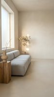 Minimalist living room interior with curved beige sofa, wooden side table, dried flowers in vase, and natural light from large window. Suitable for home decor, interior design, and lifestyle publications.