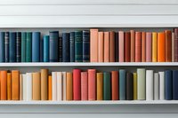 Colorful books arranged on white shelves in rainbow spectrum order, from dark blue and green to orange and red tones, creating modern minimalist library display.