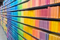 Colorful rainbow spectrum of books arranged on library shelves creating vibrant gradient pattern, modern bookstore interior with organized literature collection.