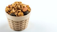 Mixed nuts and dried fruits in wicker basket on white background. Healthy snacking, organic food ingredients for cooking and baking recipes.