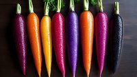 Fresh rainbow carrots in vibrant purple, orange, yellow, red and black varieties lined up on dark wooden background showing natural organic produce diversity.