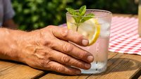 Man holding refreshing mojito cocktail with mint and lemon on wooden table outdoors, perfect for beverage, summer drink, and hospitality marketing.