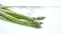 Fresh green asparagus spears splashing into clear water with bubbles, healthy organic vegetable for cooking and nutrition concepts on white background.