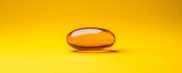 Orange transparent gel capsule or vitamin supplement pill on vibrant yellow background with soft shadow and reflection, macro photography.