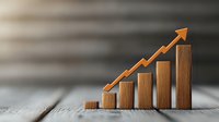 Ascending wooden blocks with orange arrow showing growth trend on rustic wooden surface against blurred background, representing business success and progress.