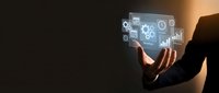Businessperson holding digital tablet displaying holographic interface with gears, charts, and technology icons for business solutions, automation, and digital transformation concepts.