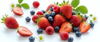Fresh mixed berries including strawberries, blueberries and raspberries with green leaves scattered on white background for healthy eating concepts.