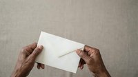 Senior adult hands holding blank white envelope against neutral beige textured background. Suitable for mail, correspondence, communication, and business concepts.