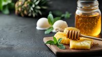 Fresh pineapple slices with honey dipper, mint leaves and jar of natural honey on dark stone background. Healthy organic sweetener concept.