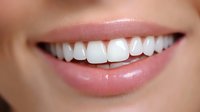Close up of bright white healthy teeth and natural pink lips showing genuine smile against soft skin background, suitable for dental and cosmetic advertising.