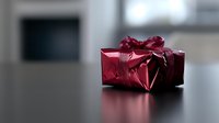 Red metallic gift box with shiny bow on dark reflective surface against blurred background, elegant holiday present packaging for special occasions.