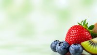 Fresh mixed berries and kiwi fruit arrangement on soft green bokeh background for healthy eating and nutrition concepts.