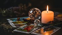 Mystical tarot cards spread with burning candle, crystal ball and dried herbs creating atmospheric fortune telling scene for spiritual guidance sessions.
