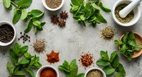 Fresh mint leaves and assorted spices arranged in a flat lay on a gray stone surface with mortar and pestle for culinary use.