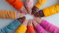 Diverse hands forming a circle, symbolizing unity, teamwork, and collaboration in colorful winter clothing against a gray background.