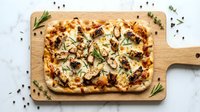 Focaccia bread with caramelized onions, mushrooms, and rosemary on wooden serving board, overhead view for food styling and culinary content.