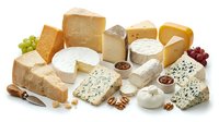 Assorted gourmet cheese selection with soft and hard varieties, nuts, grapes and crackers on white background for culinary and food photography.