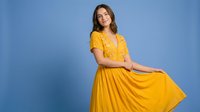Happy young Caucasian woman in bright yellow summer dress dancing and twirling against blue studio background for fashion and lifestyle content.
