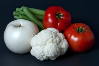 Fresh vegetables and apple on dark background, featuring cauliflower, red tomatoes, celery, and white apple for healthy eating concepts.