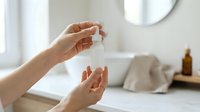 Woman applying skincare serum or facial oil from dropper bottle in modern bathroom, self-care and beauty routine.
