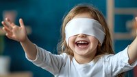 Joyful Caucasian girl wearing white blindfold, arms outstretched with excited expression and big smile against blue background. Fun childhood game concept.