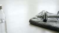 Chrome dumbbell resting on gray towel with water bottle, representing fitness, workout routine, strength training, and healthy lifestyle for gym and wellness design projects.