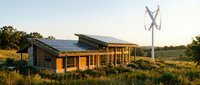 Modern eco-friendly house with solar panels and wind turbine in rural landscape at sunset showcasing sustainable green energy technology and off-grid living.