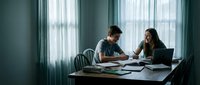 Young diverse couple working together at home office desk with laptop and documents, collaborating on business project in modern interior with natural light.