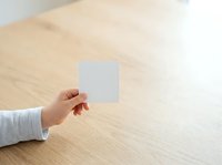 Cropped hand holding blank white card on wooden table surface, suitable for business branding, marketing mockups, and corporate identity presentations.