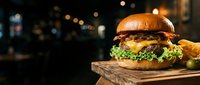 Gourmet burger with melted cheese, fresh lettuce and crispy fries on wooden board against blurred night lights, ideal for restaurant menus and food marketing.