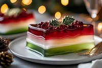 Layered holiday jelly dessert with red cranberries and holly decoration on plate against festive bokeh lights background, Christmas party food styling.