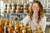 Caucasian female small business owner with long wavy hair smiling while arranging bottles in artisanal food store, warm lighting highlights retail display.