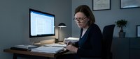 Professional businesswoman working late at office desk with computer and documents in modern workplace setting for corporate productivity concepts.