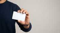 Cropped view of male hand holding blank white business card against neutral background for corporate branding and marketing purposes.