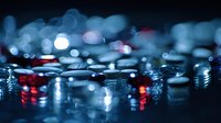 Macro photography of water drops with red and blue bokeh lights creating atmospheric night city reflection effect on dark background. Artistic abstract composition.