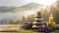 Zen stone stack with lavender flowers and burning candle at sunrise in mountain landscape for meditation wellness spa relaxation mindfulness balance harmony.