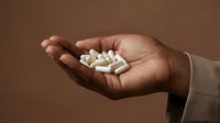 Hand holding white capsule pills and tablets on neutral brown background for healthcare and medicine concepts.