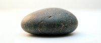Smooth dark gray river stone with natural texture and weathered surface isolated on white background for spa wellness meditation design projects.