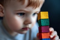 Young Caucasian boy with blue eyes and light hair stacks colorful wooden blocks while developing fine motor skills and concentration. Educational preschool activity.