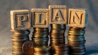 Wooden letter blocks spelling PLAN stacked on coin piles representing financial planning, budgeting, investment strategy and wealth management concepts.