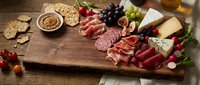 Gourmet charcuterie board with assorted meats, cheeses, crackers, grapes and nuts on rustic wooden surface for entertaining and appetizer presentations.