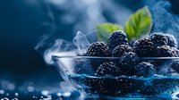 Fresh blackberries in glass bowl with rising steam against dark blue background, dramatic lighting creates mysterious atmosphere for food photography.