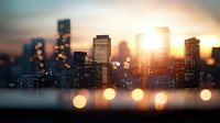 Blurred city skyline silhouette at sunset with golden bokeh lights in foreground creating dreamy urban landscape atmosphere.