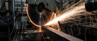 Industrial metal grinding machine creating bright orange sparks in manufacturing workshop. Heavy machinery metalworking process for fabrication projects.
